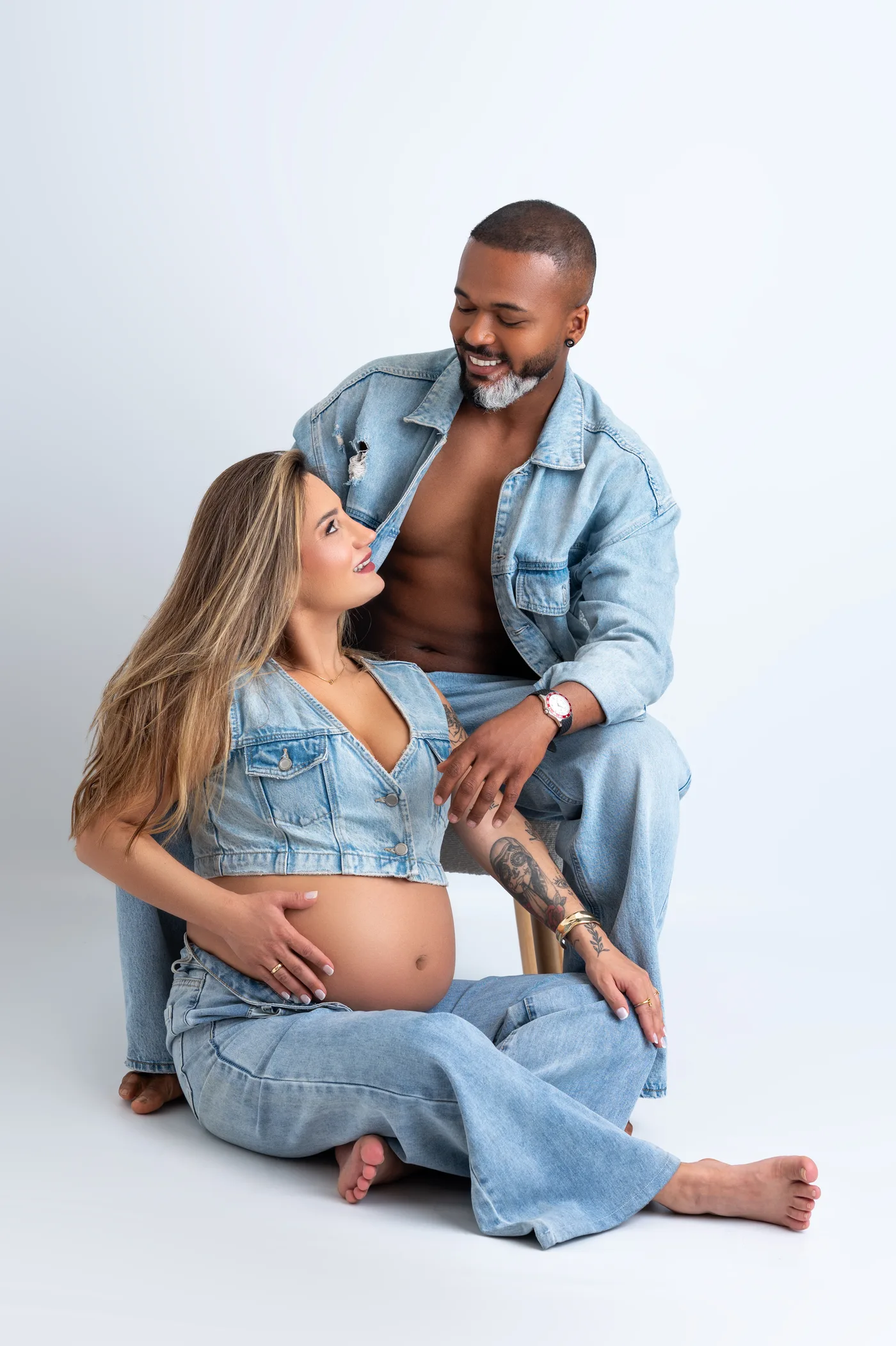 Casal de jeans sentado no chão, ela grávida encostada nele